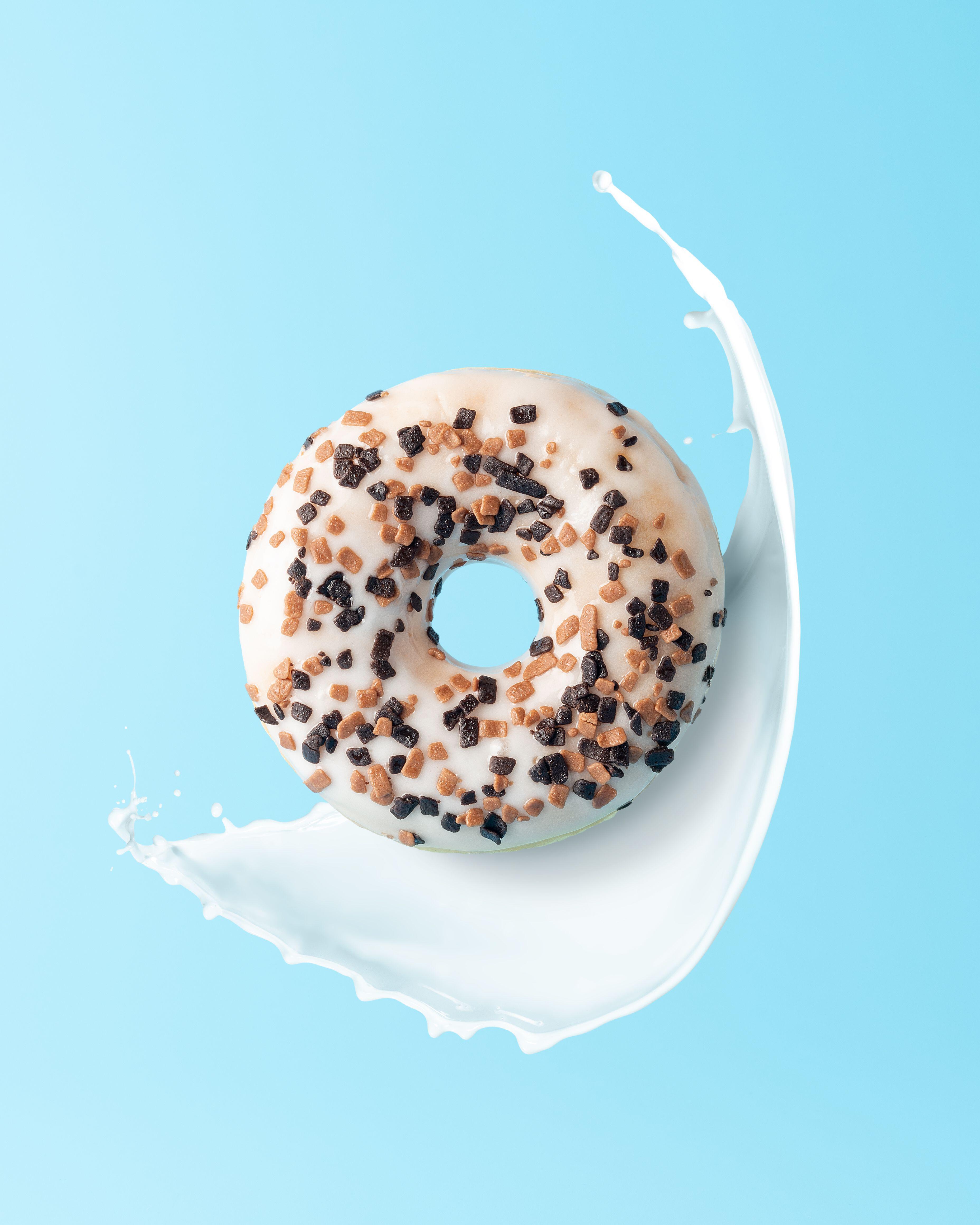 Fresh donut with milk splashes on blue background. Minimal food concept.